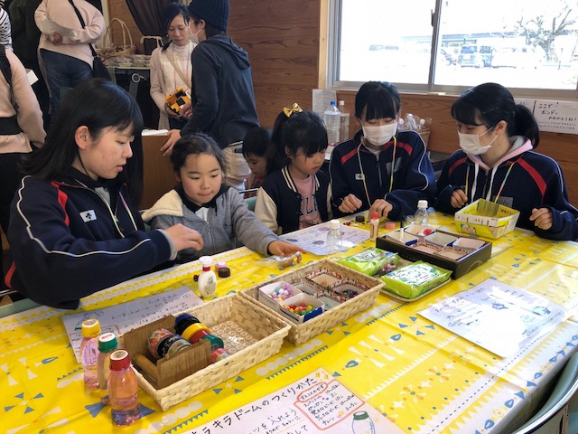 3人の高校生に手伝ってもらいながらキラキラドームづくり体験をしている2人の女の子の写真