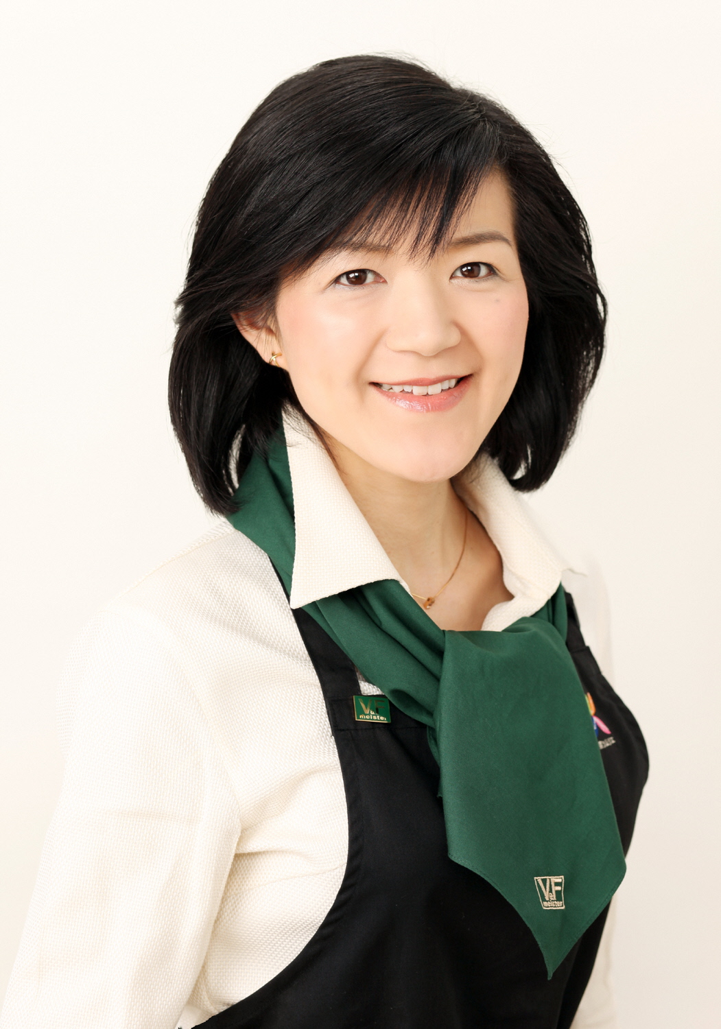 エプロンを付け、緑色のスカーフを巻いた中沢るみ氏の写真