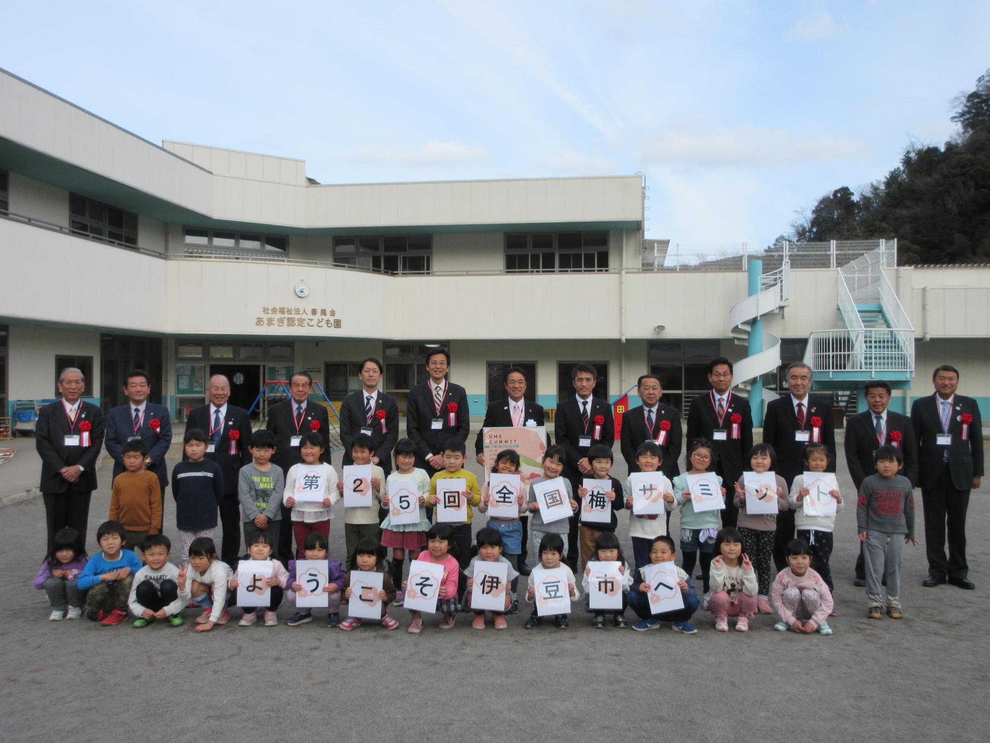 梅サミット協議会加盟市町の代表者の方々と、「第25回全国梅サミット ようこそ伊豆市へ」と書かれたカードを持ったあまぎ認定こども園の園児との記念写真