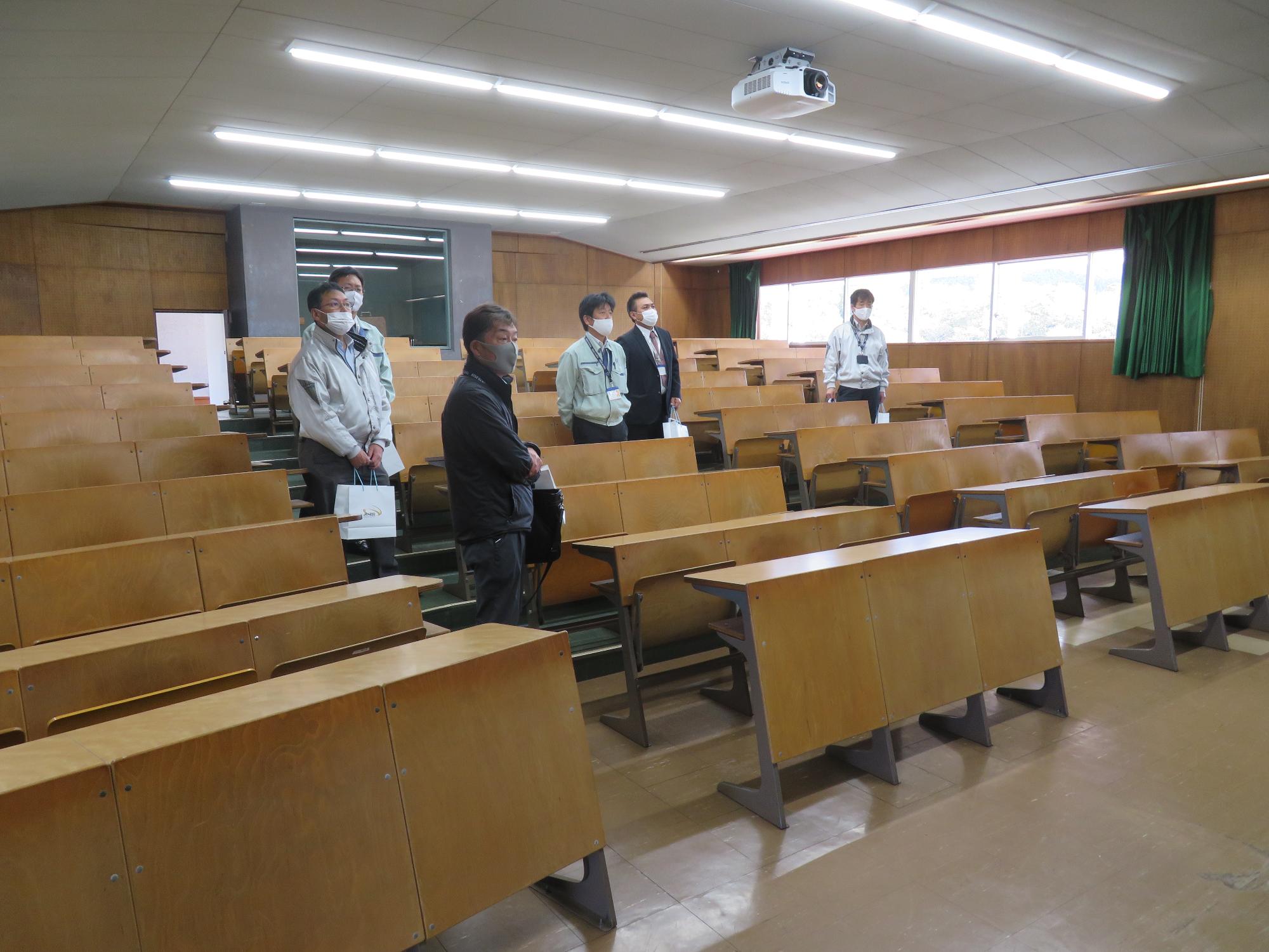 長机が並んだ視聴覚室の室内を職員達が見学している写真