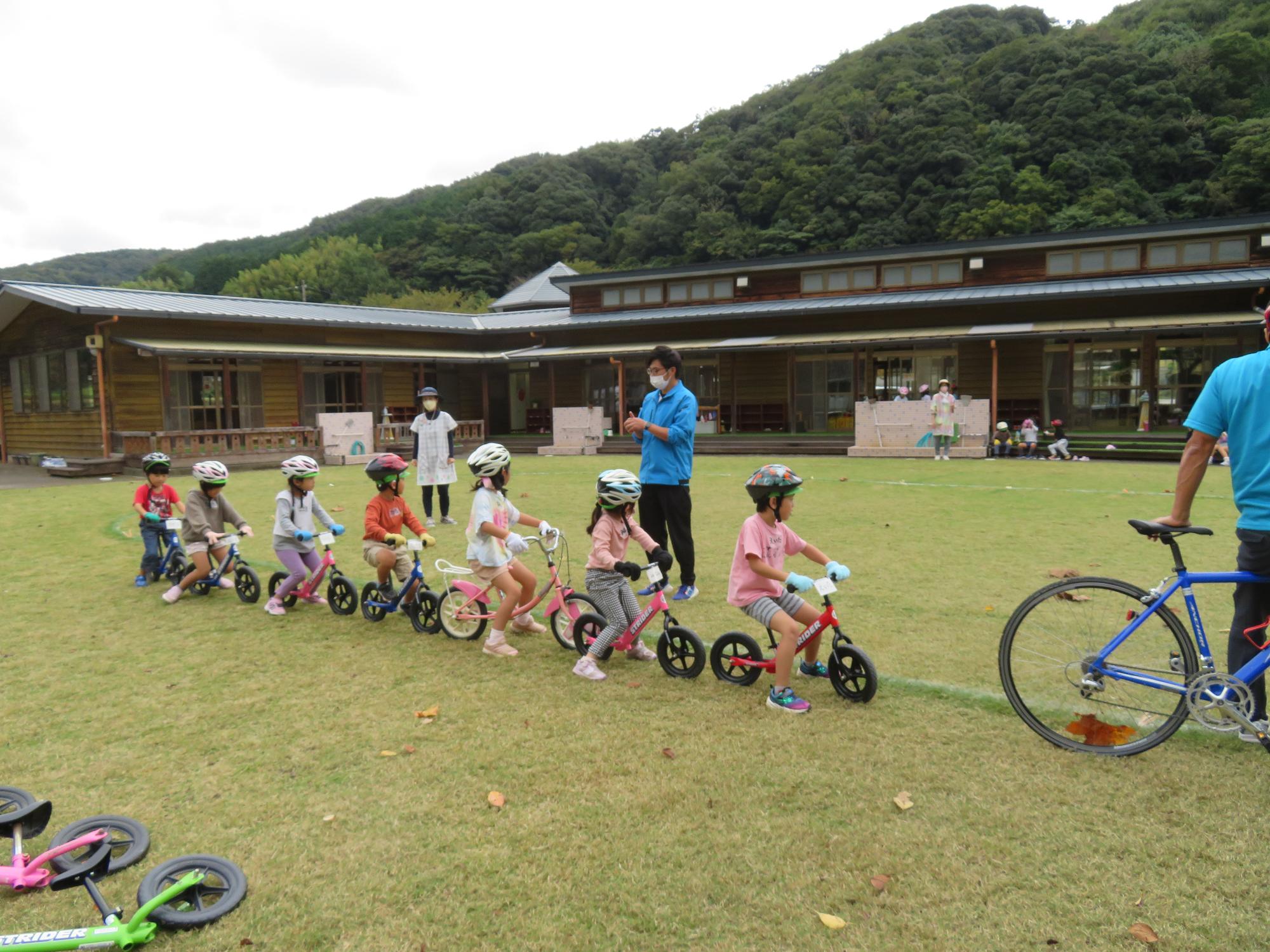 芝生の広場でヘルメットを被り自転車にまたがった7名の子供たちが縦に並んでいる写真
