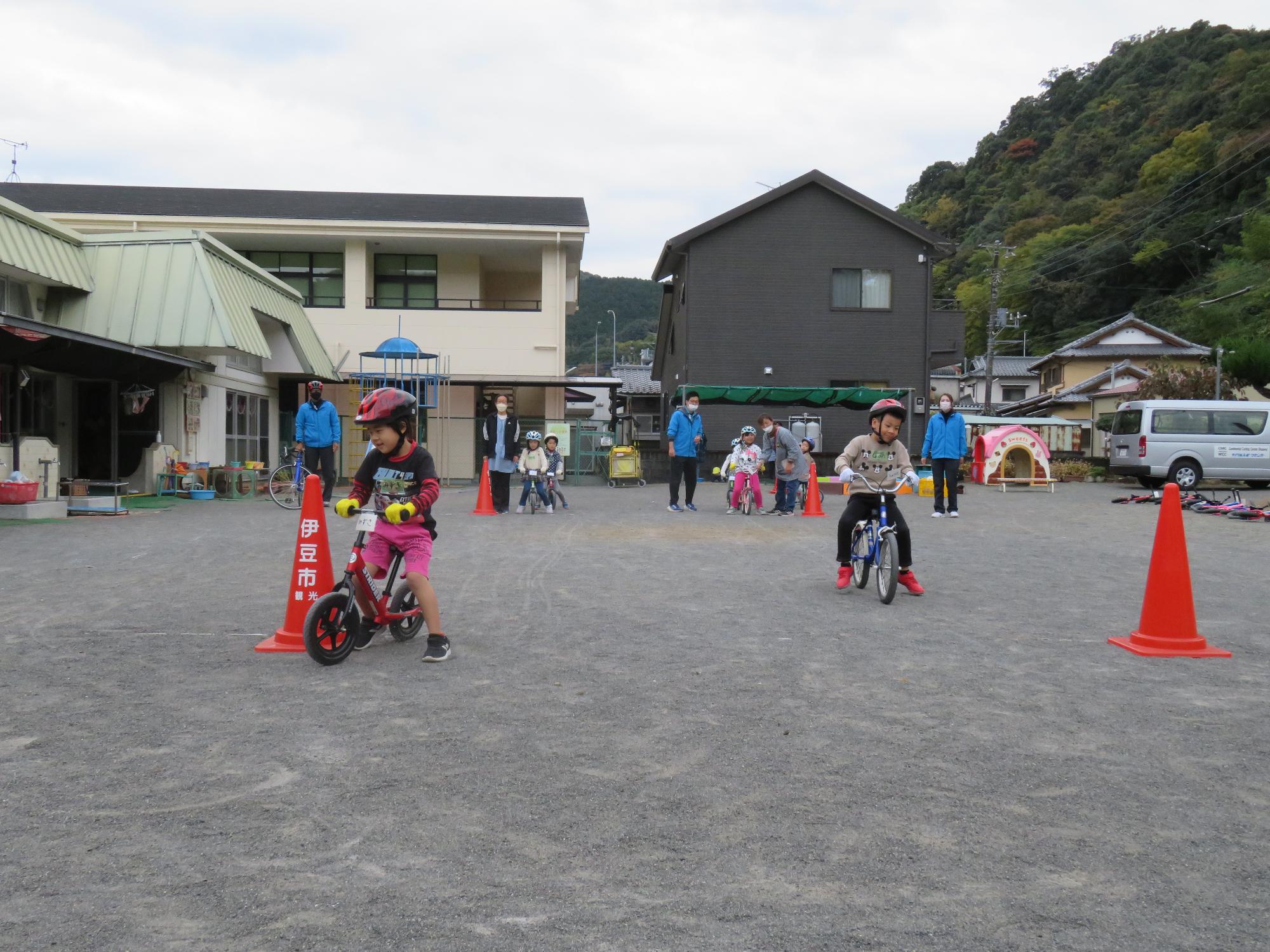 ヘルメットを被った子供たちが地面に置かれた2つの赤いコーンの間を自転車で通っている写真