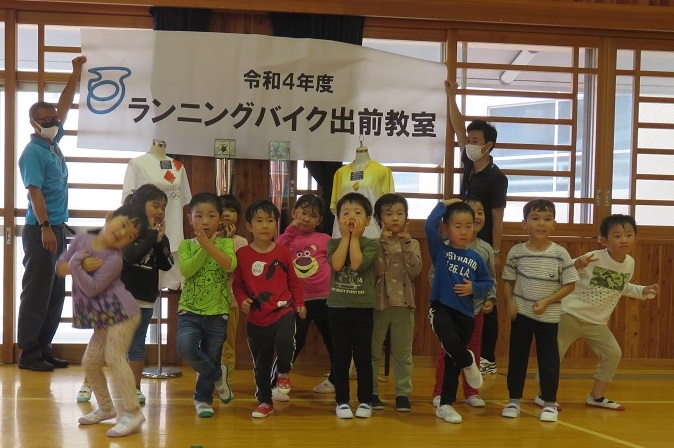 令和4年度ランニングバイク教室と書かれた幕の前で土肥こども園の子供たちが並んでいる集合写真
