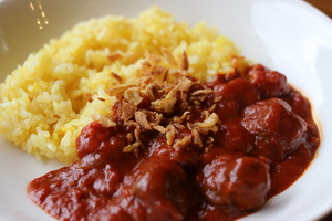 黄色く色づくライスの横にごろごろとしたお肉が入ったトマトカレーが盛り付けられている写真