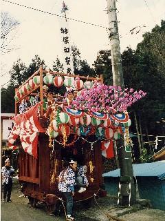 提灯や紅白幕、梅の花などで飾られ、中に法被を着た人が複数人乗っている花車の写真