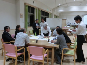 テーブル席に参加者が座り話をし、1人の男性が資料に書き込みをしている様子の写真