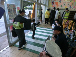 横断歩道を模したシートの上を手をあげてわたる新入学児と着物を着た女性の写真