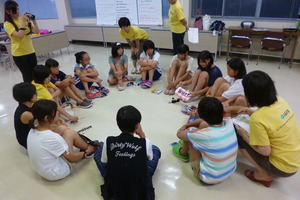 輪になって座っている学生の周りや、隣に黄色いシャツを着た女性たちが座っている写真