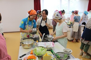 調理器具や材料が置かれたシンクの前に立ち、作業をしながら談笑する女性参加者と講師の写真