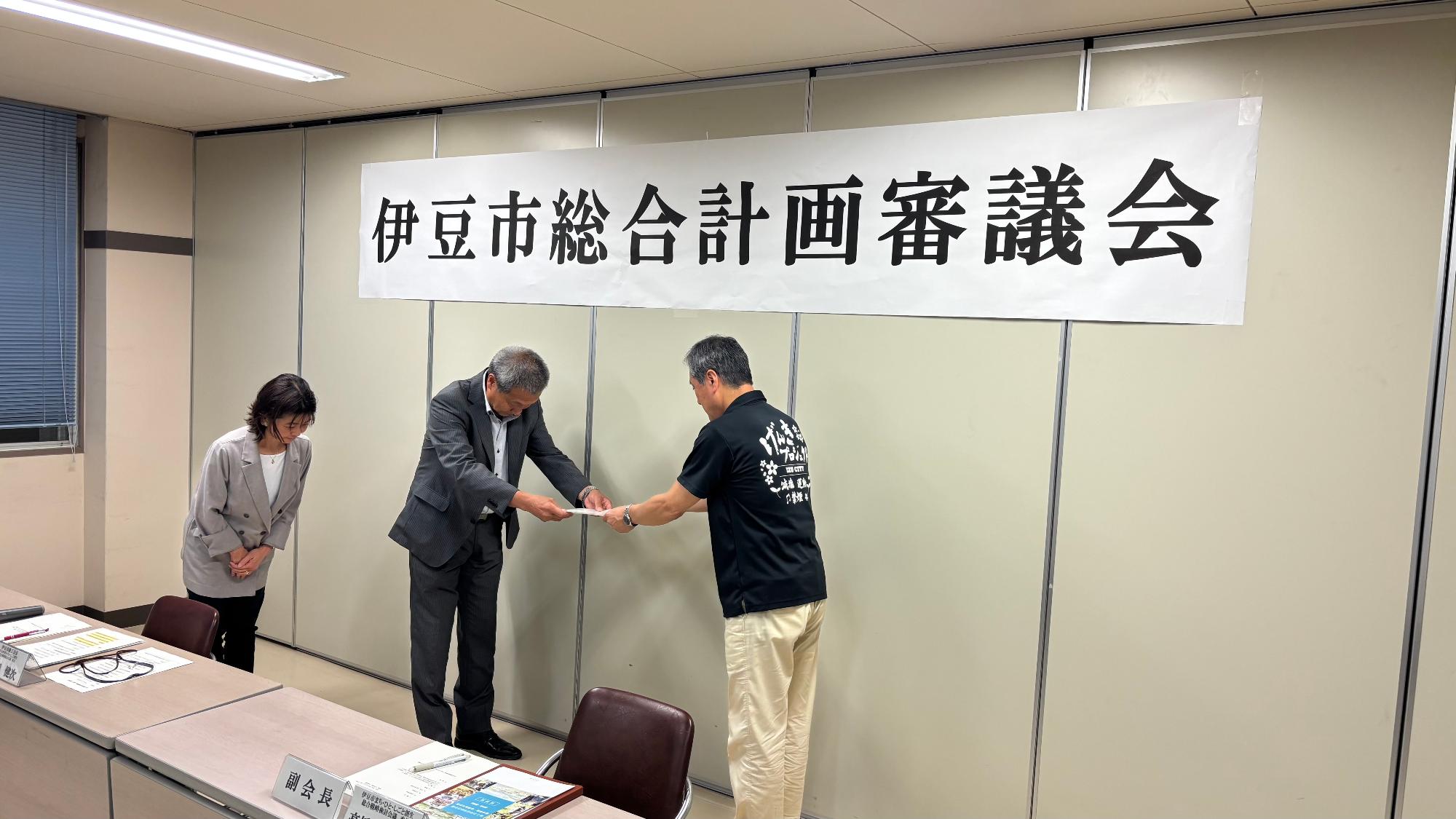 市長が山田会長に諮問書を手渡しする様子を右側から撮影した写真