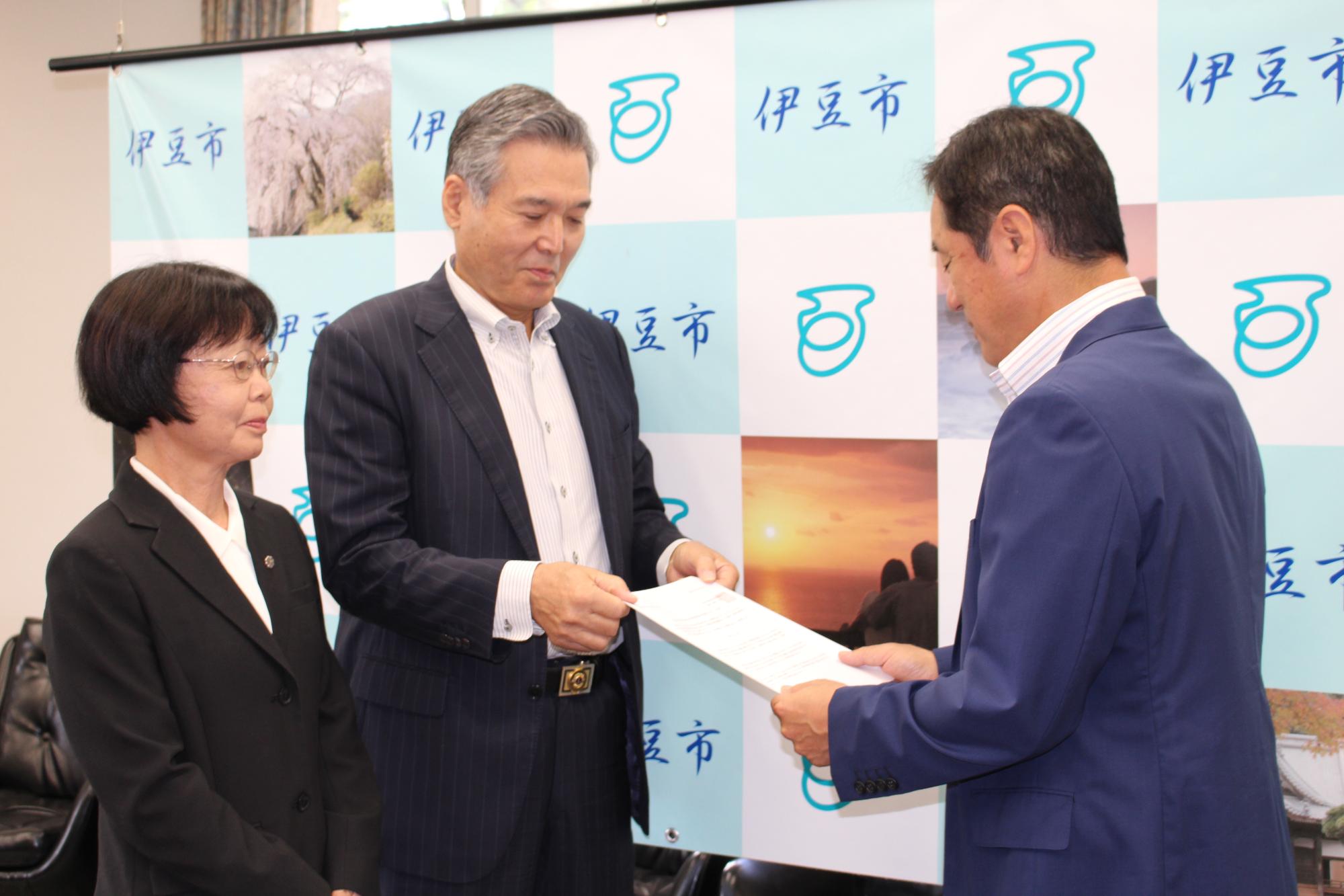 飯田会長・内田副会長が横に並び、飯田会長が市長に答申書を手渡している様子の写真