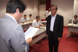 市長が諮問書の内容を読み上げ、正面に立つ遠藤会長がそれを聞いている写真