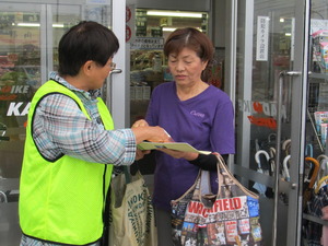 スーパーから出てきた女性にビブスを着た食育推進会議委員が市の食育PRのチラシを配っている写真