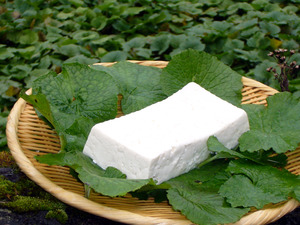 木ざるの上の緑の葉っぱの上に真っ白な豆腐がのせられている写真