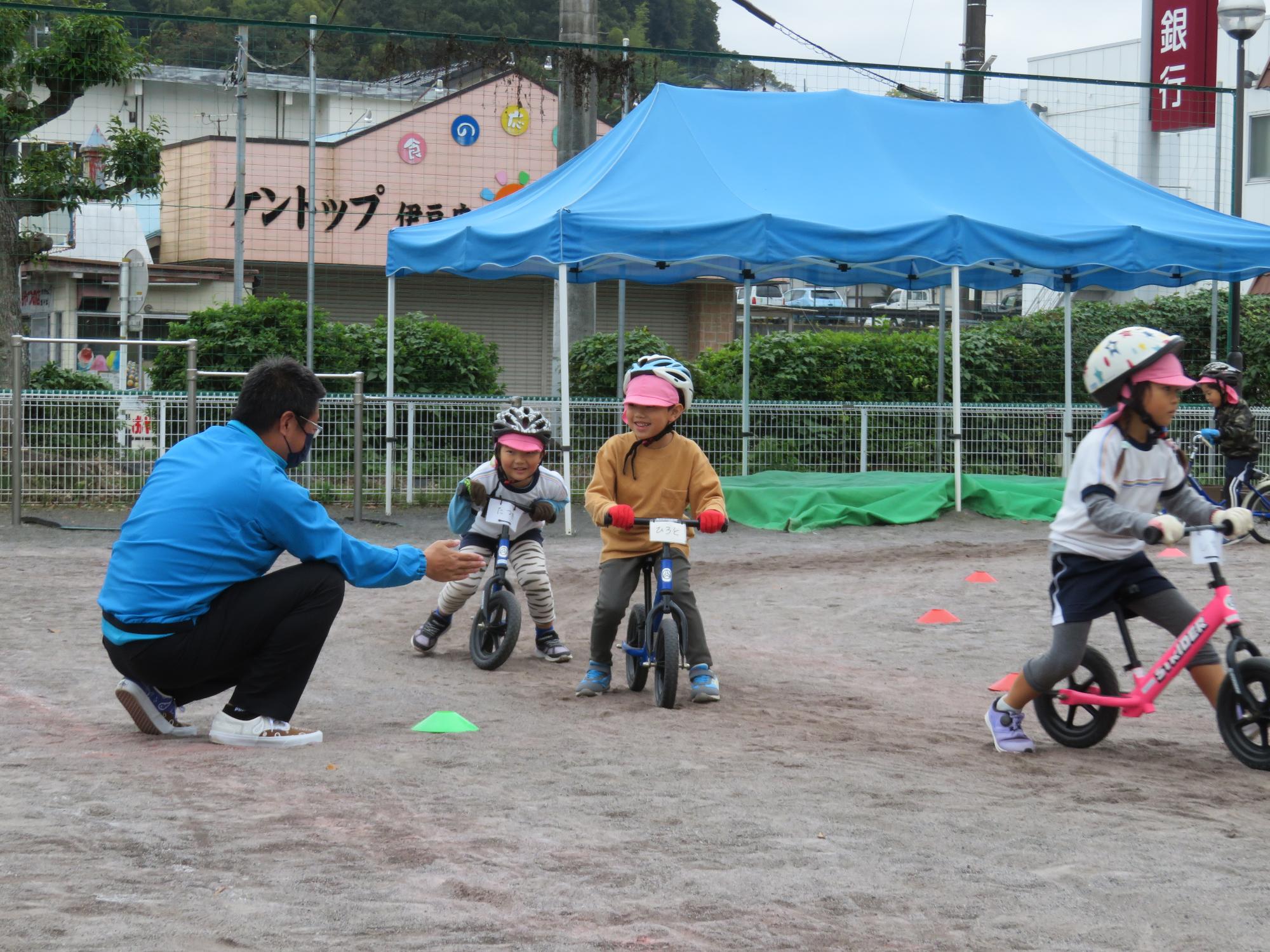 ヘルメットを被って自転車にのった子供2名が横にしゃがんでいる男性と話しながら笑っている写真