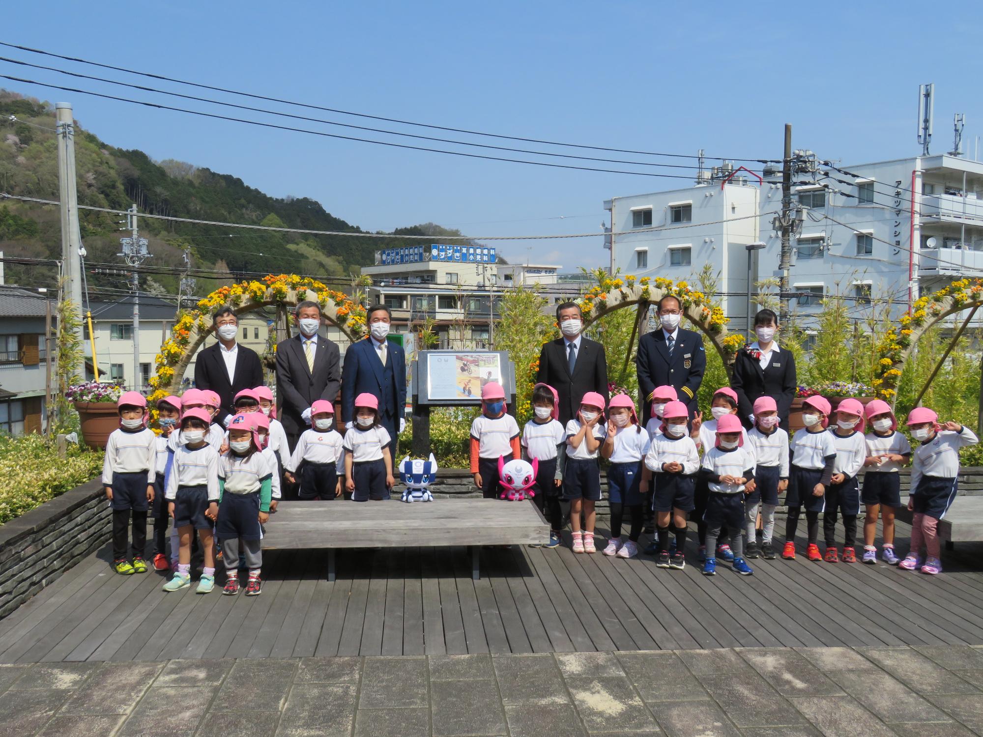 修善寺駅北口花壇前にレガシー銘板が設置され、その前に並んでいる園児や関係者の記念写真