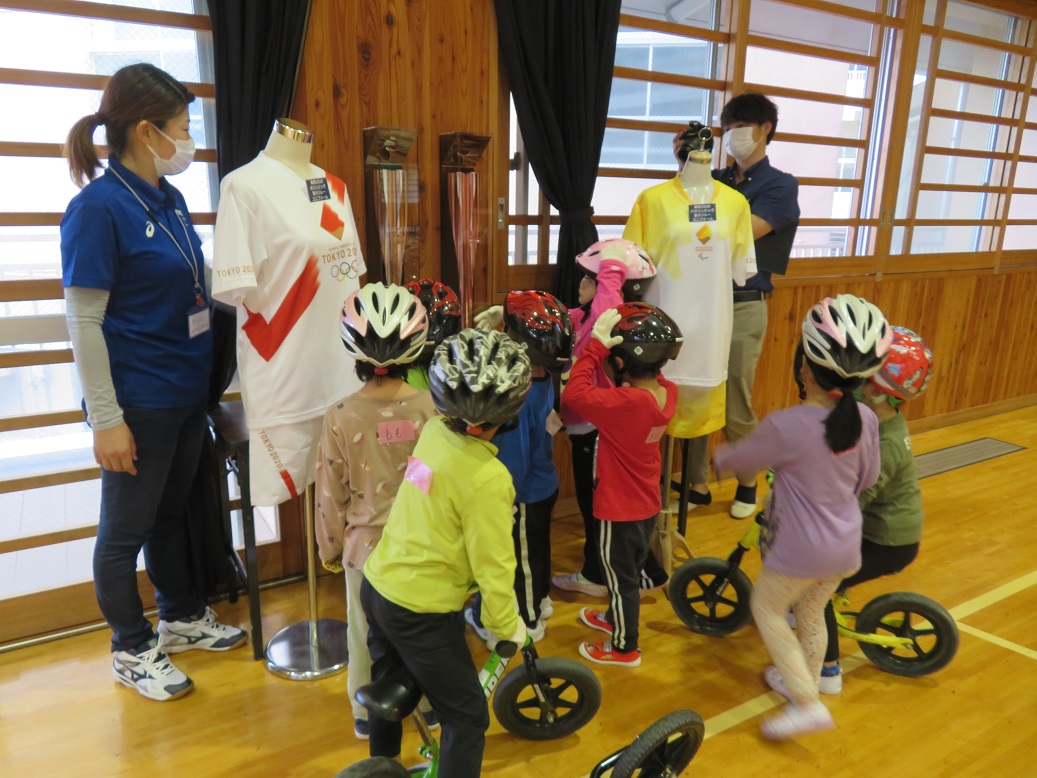 ヘルメットを被った子供たちが展示されている2着のユニフォームを見ている写真