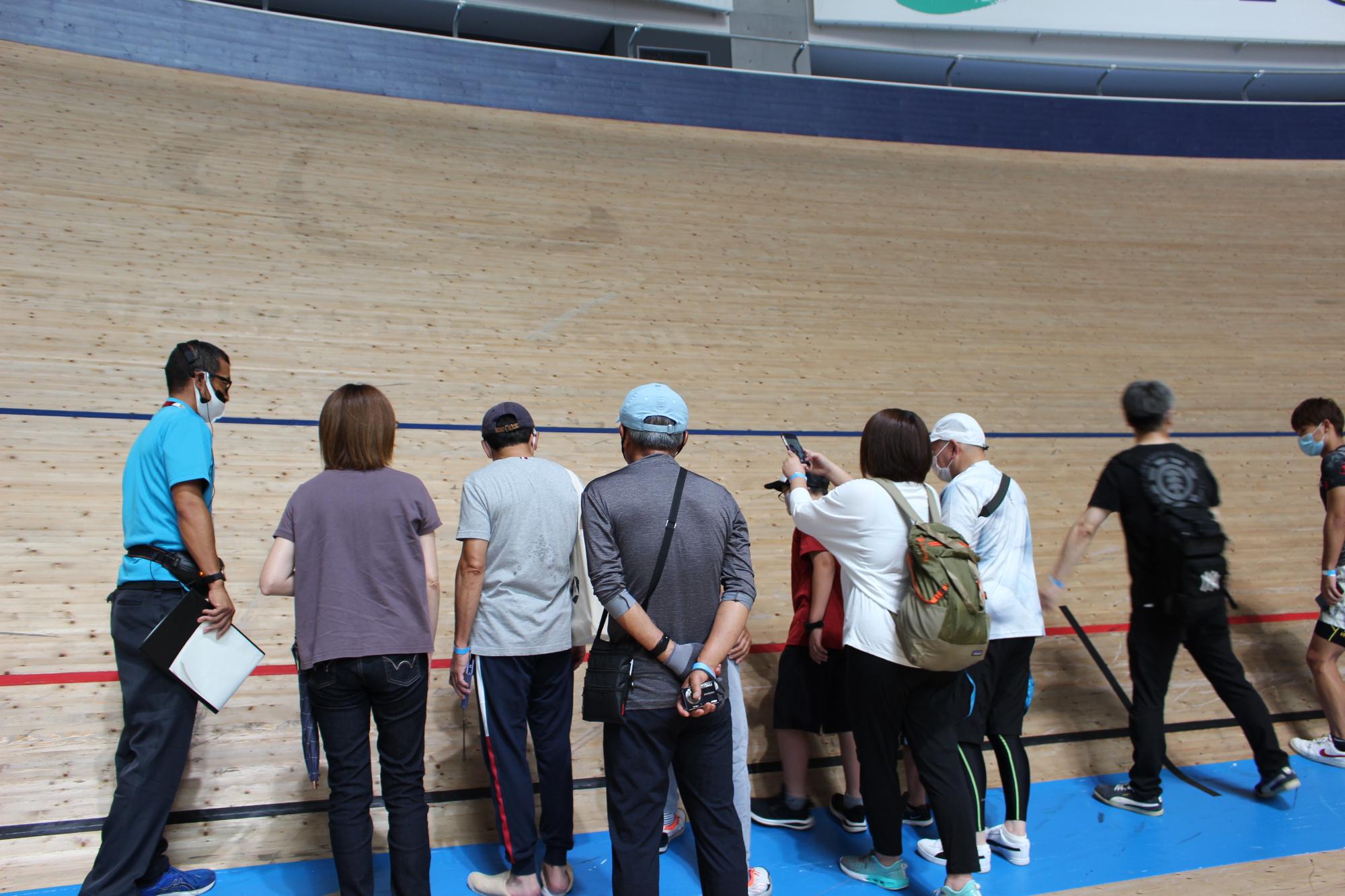 壁のような傾斜の木製トラックの前に立ち写真を撮ったり近くで見ている参加者の写真