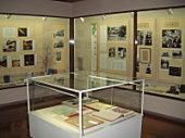 中央に置かれたガラスケースに原稿が展示され、周りの壁に沢山の写真が展示されている室内の写真
