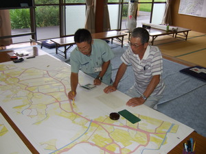 大きな地図を机の上に広げ、男性2名がペンを使って地図を指し確認している様子の写真