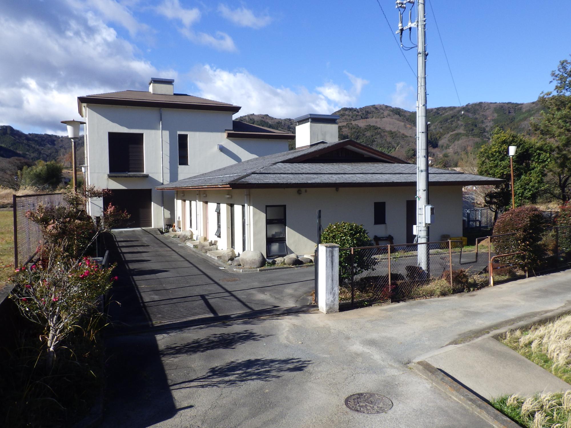山に囲まれ、手前に平屋、後ろに2階建ての佐野雲金処理場の外観写真