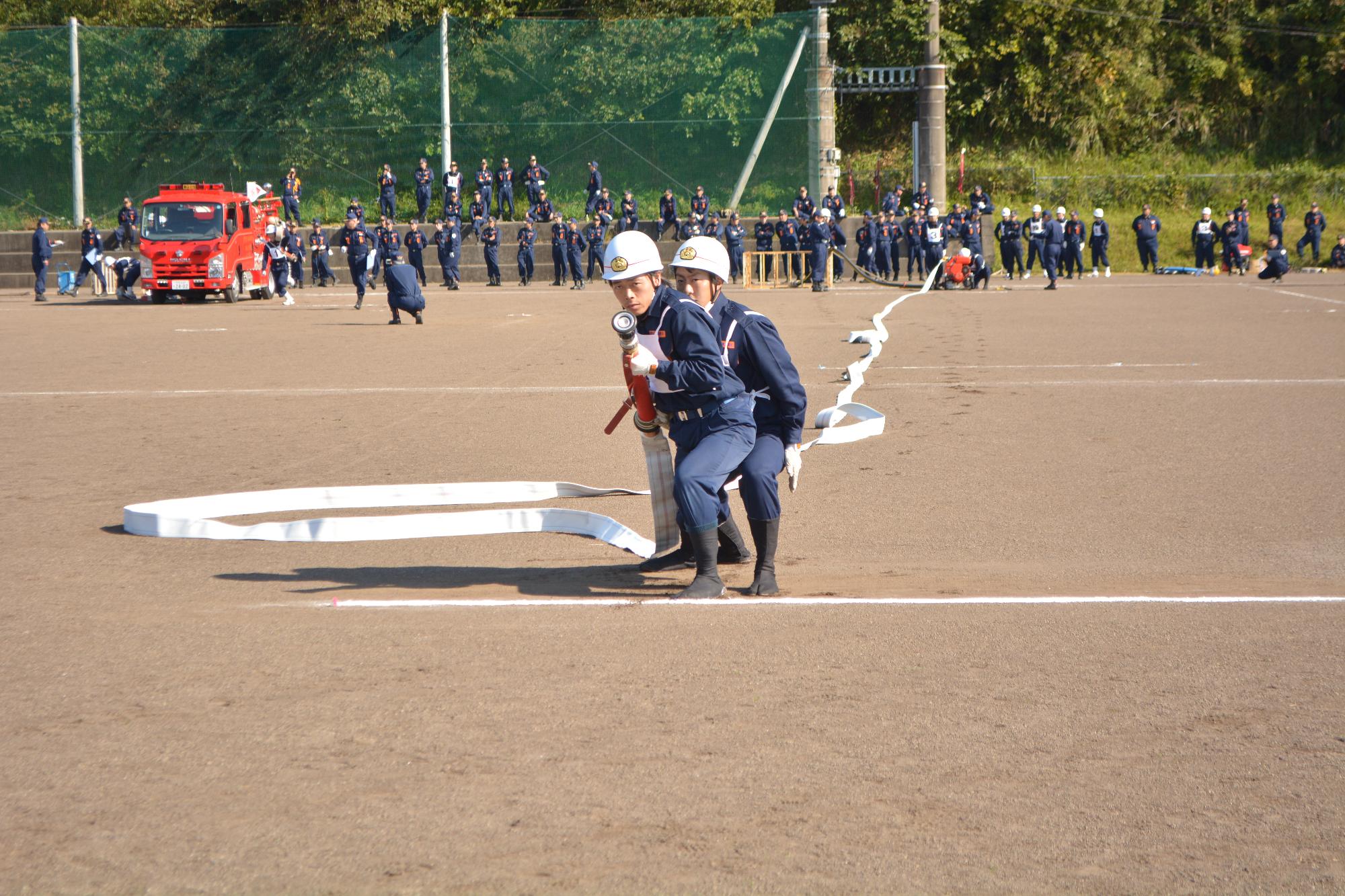 ヘルメットを着用した隊員2名が消火活動に使用するホースを手に持ち放水訓練を行っている写真
