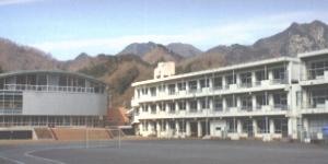 左側に体育館、右側に3階建ての校舎が2棟横並びに立っている熊坂小学校の写真