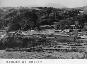 手前に年川前田遺跡がうつり、奥に家々や木々が写っている白黒写真