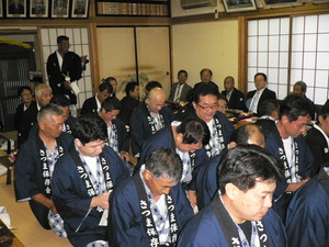 畳の部屋に紺色の法被を着た男性達がぎっしりと座っている写真