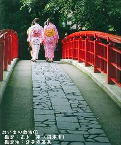 ピンクと白の浴衣を着た女性が橋を散歩している様子を後ろから撮影した写真