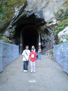岩を切り出して作られた縦長の大きなトンネルの前に2人の男の子が立っている写真