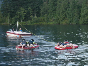 ボードから伸びたロープに括り付けられた大きな浮き輪のようなものに落ちないようにしがみつき遊んでいる救命胴衣を着た子供たちの写真