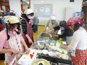 エプロン、三角巾を付けた5名の女性が調理をしている写真