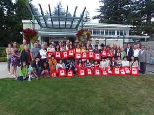 赤枠で囲まれたカナダの国旗が描かれたボードを持った生徒たちとホストファミリーらの集合写真