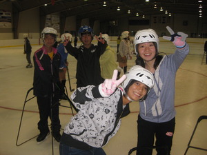スケートリンクでヘルメットを付けた4人の生徒たちがこちらを向いてピースをしている写真