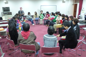 円をかいて並べられた椅子にそれぞれプレゼントを持った参加者の方々が座っている写真