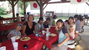 ウェルカムパーティーで、赤いテーブルクロスがひかれた席で食事をしている外国人や参加者の写真