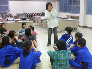 床に座っている学生が、両手で顔を触りながら立っている女性の方を注目している写真