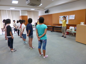 黄色いシャツを着た女性が、学生の前に立ち両手を大きく広げている写真
