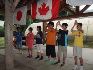 日本とカナダの国旗が掲げられたウェルカムパーティーの会場で6人並んで出し物を披露する参加者の写真