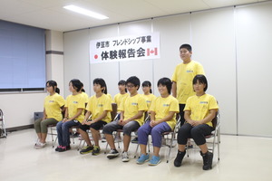お揃いの黄色いTシャツを着た生徒たちが2列に並んで座り、後列右端の男の子が立って発表をしている様子の写真